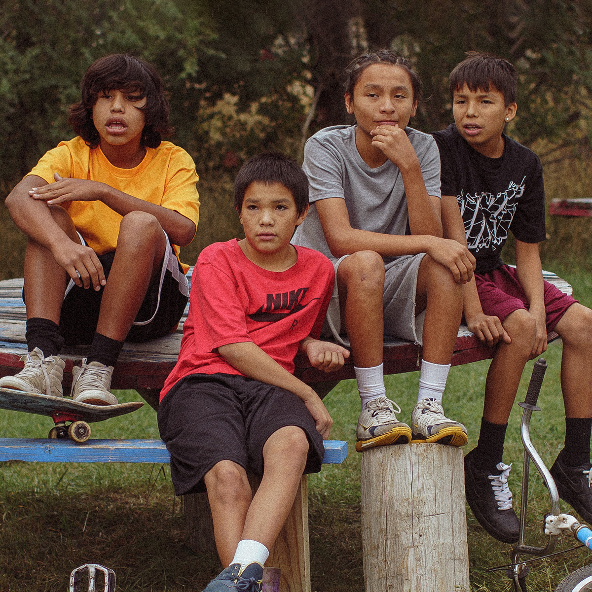 Fyra ungdomar med cyklar och skateboard sitter utomhus,