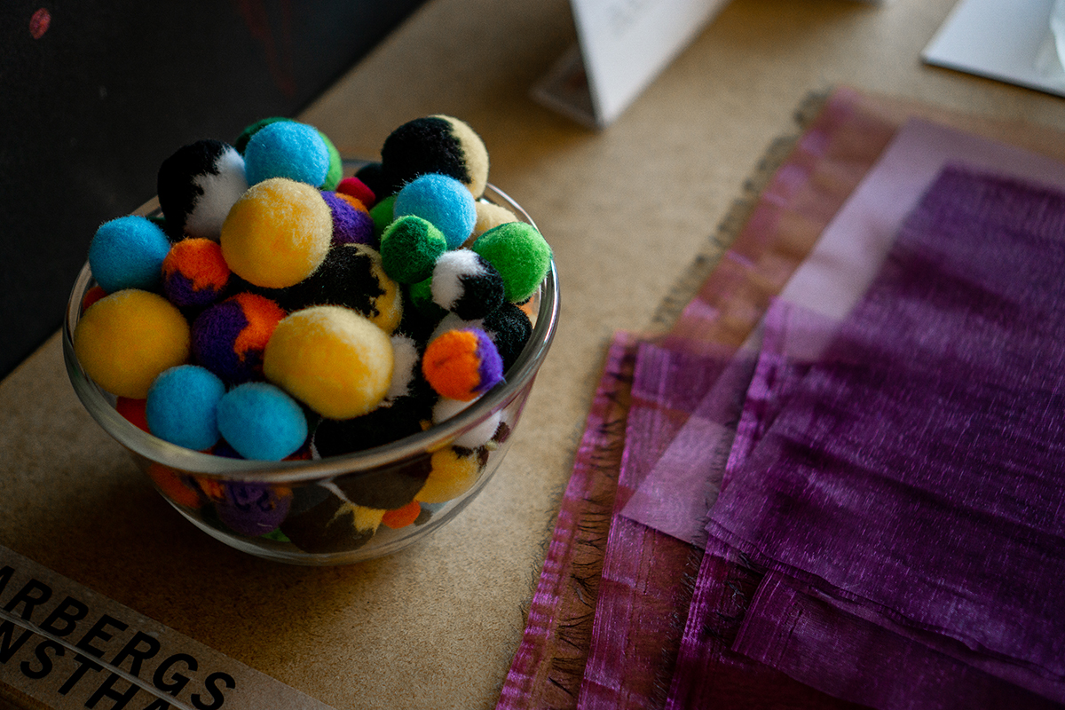 En skål med tovade bollar i olika färger bredvid en liten hög med tygstycken.