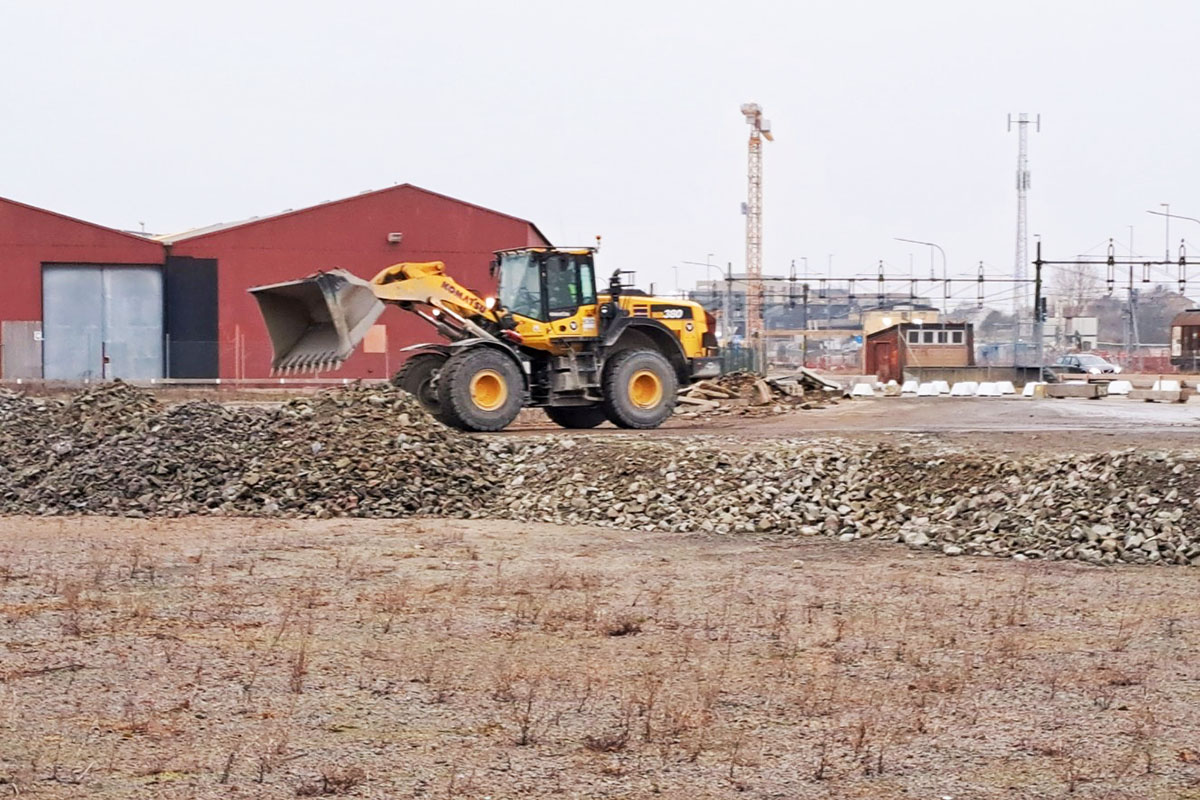 Gul grävskopa lastar av ett lass med krossade bergmassor på marken i området för Västerports första etapp i hamnen.